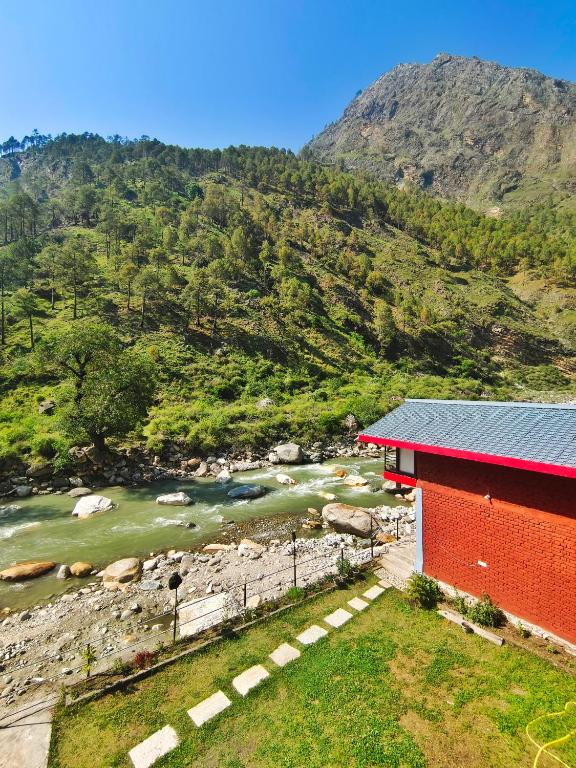 a red building next to a river next to a mountain at Riverside Bliss Cottages in Gushaini