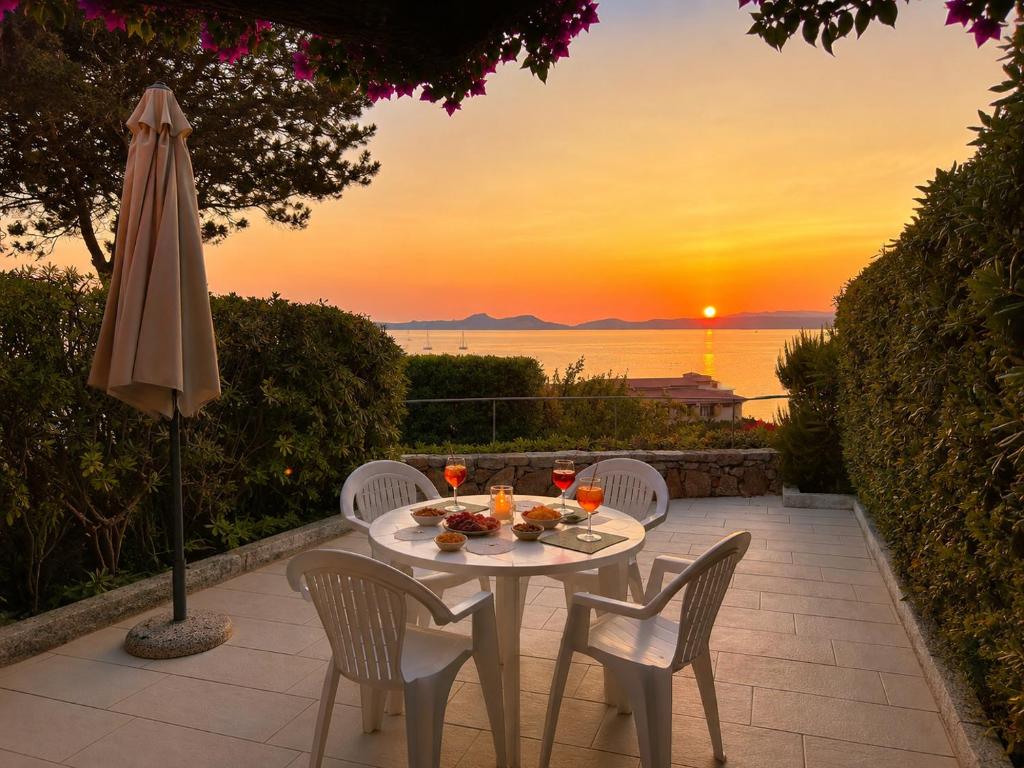 a table with chairs and an umbrella and the sunset at Sunset Three Shared Pool 100m from the Beach in Baja Sardinia