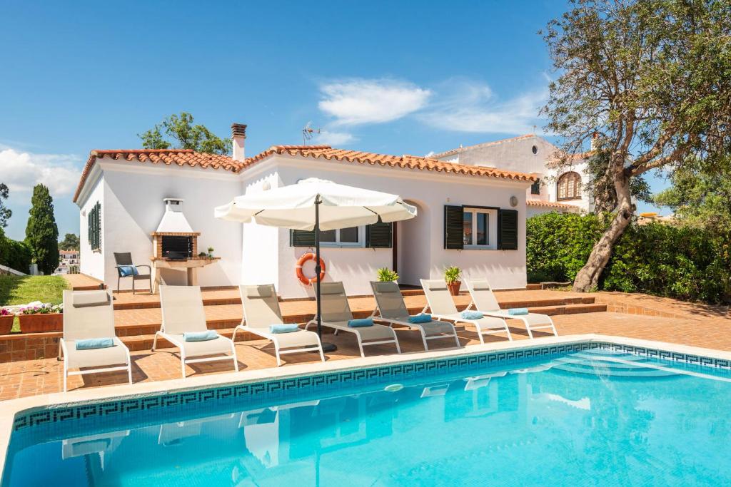 a villa with a swimming pool with chairs and an umbrella at Villa Verano in Cala Galdana