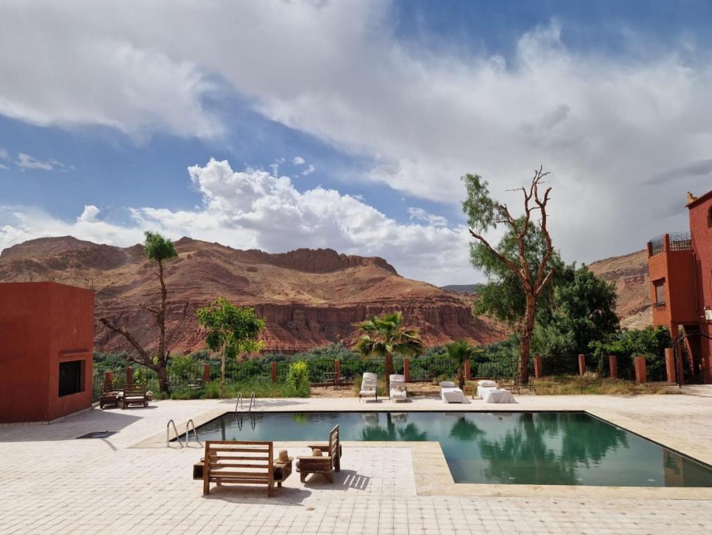 a swimming pool with benches and mountains in the background at Kasbah Chems in El Kelaa des Mgouna