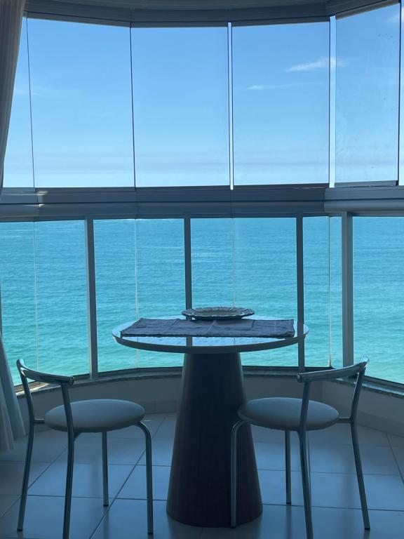 a table and chairs in front of a large window at FLAT frente Mar Green Diamond in Vila Velha