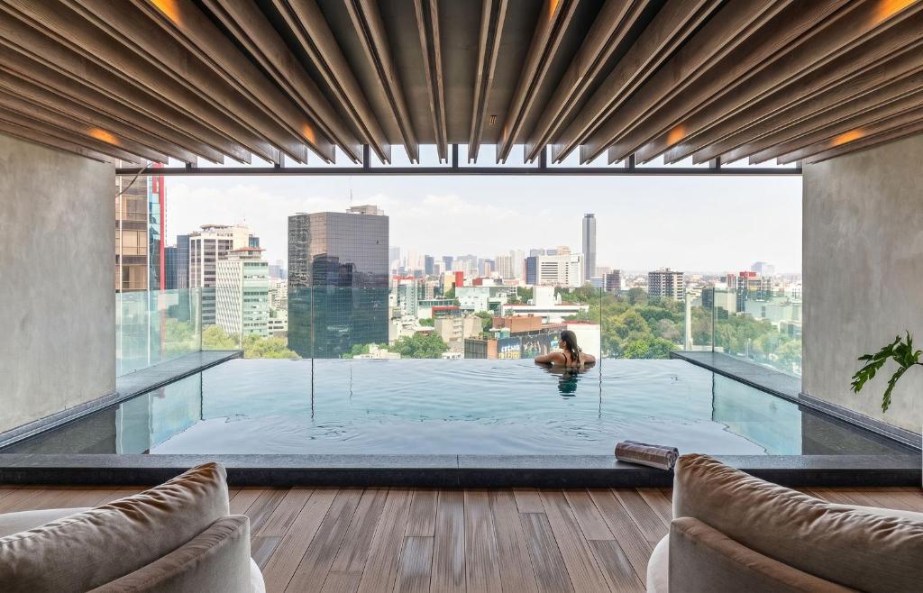 a woman in a swimming pool with a view of the city at University Tower by Kukun Apartments in Mexico City