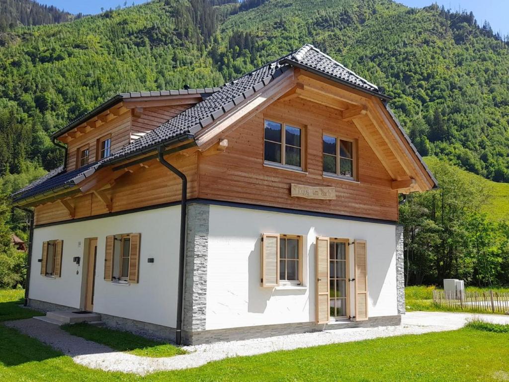 a house with a wooden roof on a grass field at Haus am Bach in Donnersbachwald