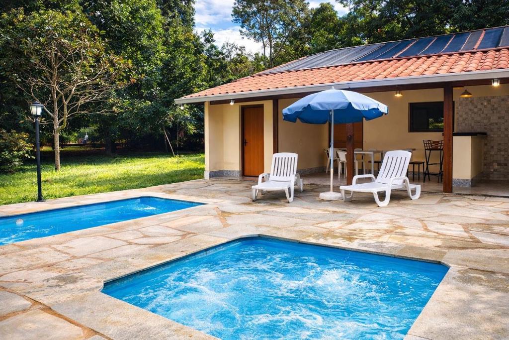 a swimming pool with two chairs and a table and an umbrella at Chalé Veredas e Buritis in Pirenópolis