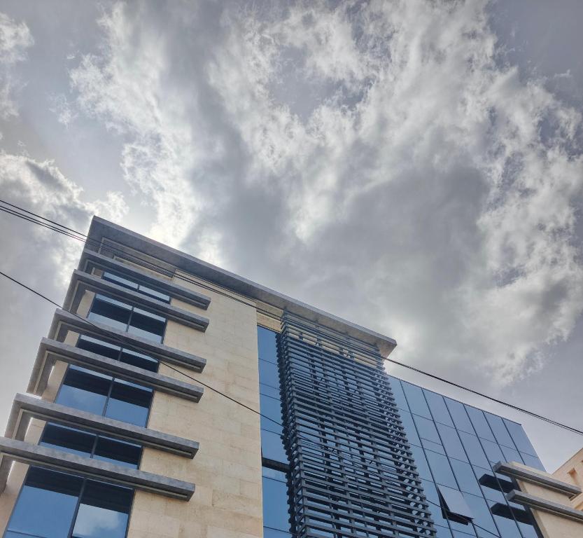 a tall glass building with a cloudy sky in the background at Hodoon Apartments in Amman