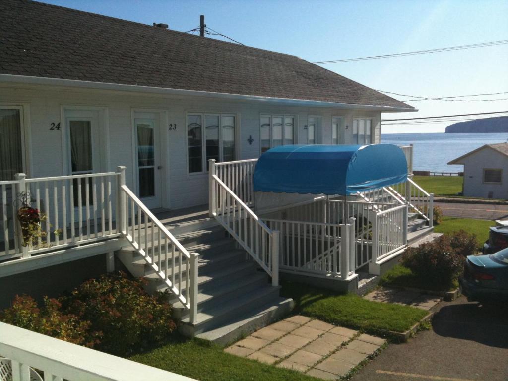 a house with a porch with a blue umbrella on it at Hotel-Motel Fleur de Lys in Perce