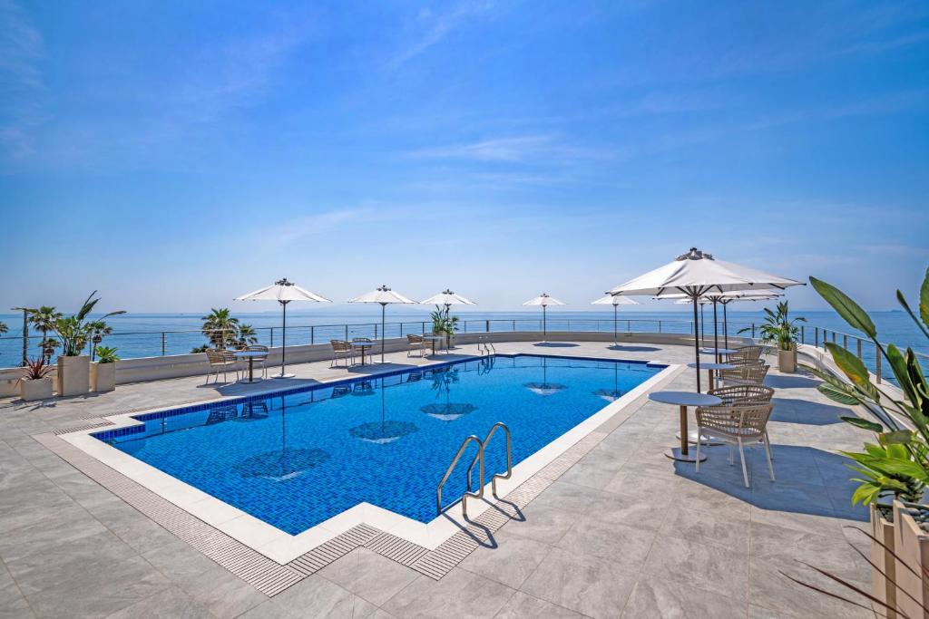 a swimming pool with tables and umbrellas next to the ocean at Atagawa Ocean Resort in Higashiizu