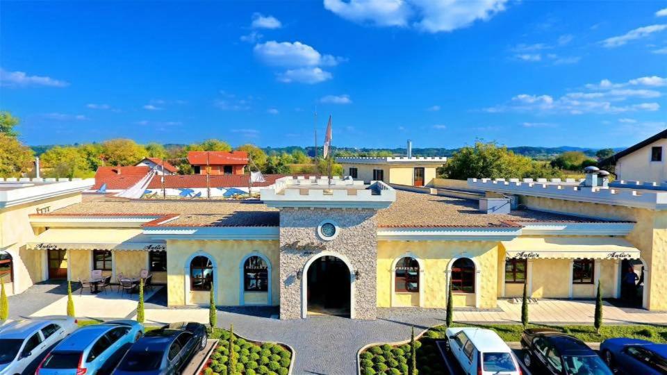 un bâtiment avec des voitures garées dans un parking dans l'établissement Motel pizzeria Antic's, à Laktaši