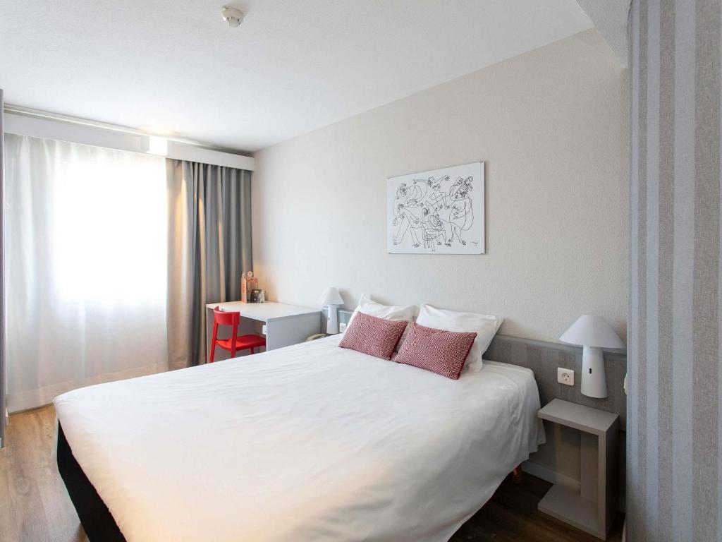 a hotel room with a white bed with pink pillows at Ibis Valencia Alfafar in Alfafar