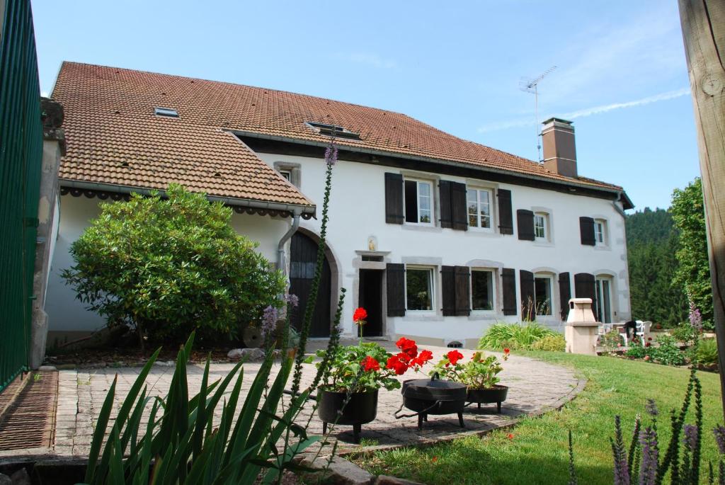 een wit huis met rode bloemen in een tuin bij Chambre d'hôtes Kieffer Le Grand Bienfaisy in Remiremont