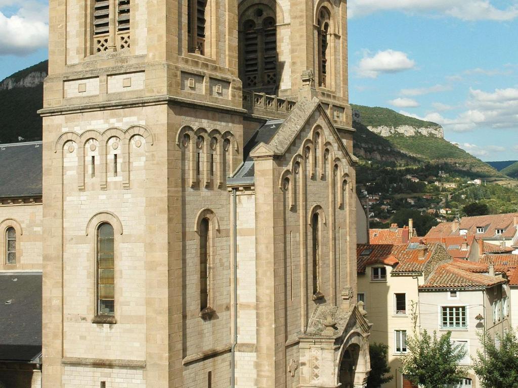 Un edificio alto con una torre de reloj frente a una ciudad. en Mercure Millau, en Millau