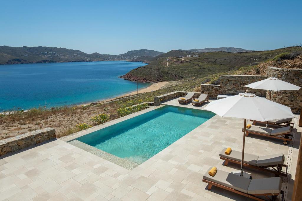 a swimming pool with an umbrella and a view of the water at Villa Sozon Mykonos in Agios Sostis Mykonos