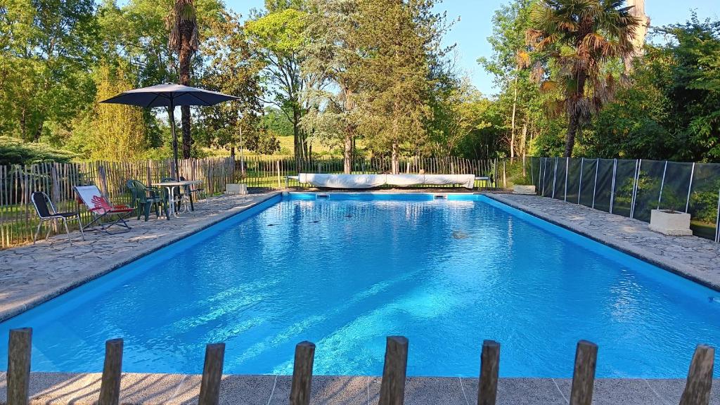 a swimming pool in a yard with an umbrella at Le Moulin du Comte - chambres privées en gîte in Bourrouillan