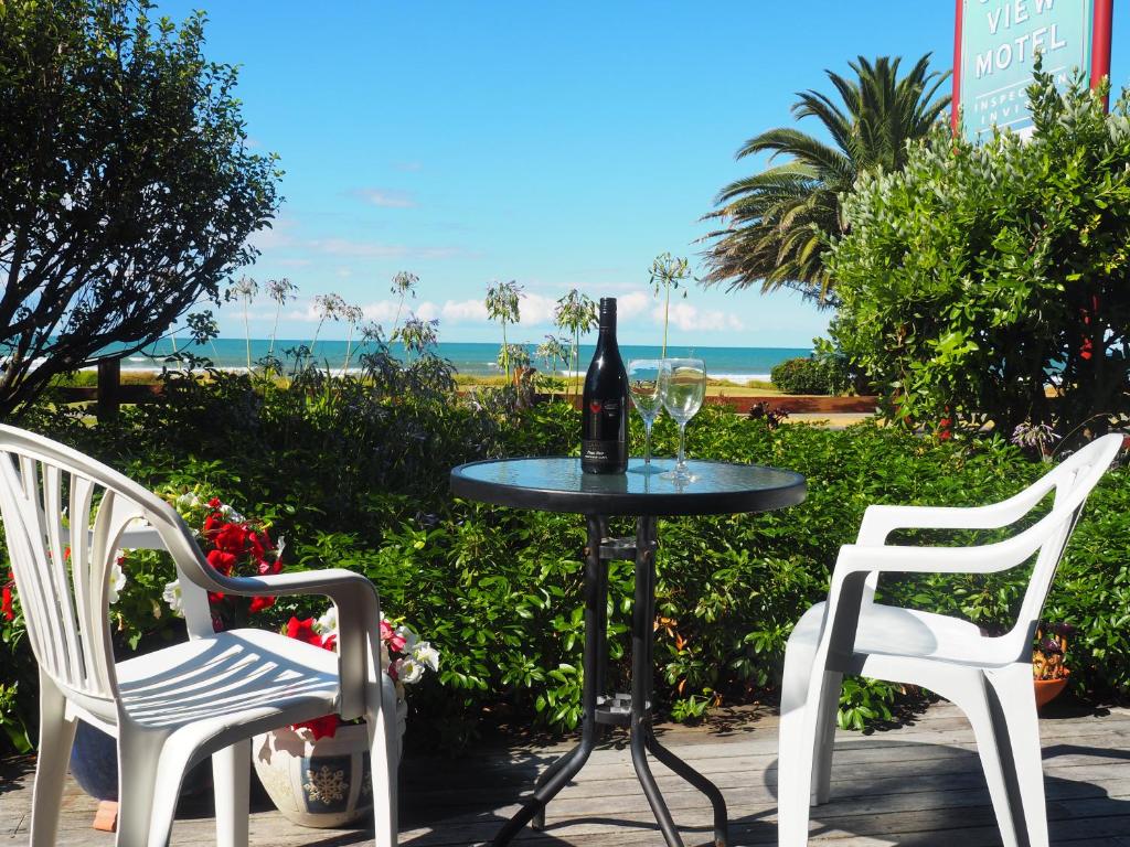a table with a bottle of wine and two chairs at Ocean View in Ohope Beach