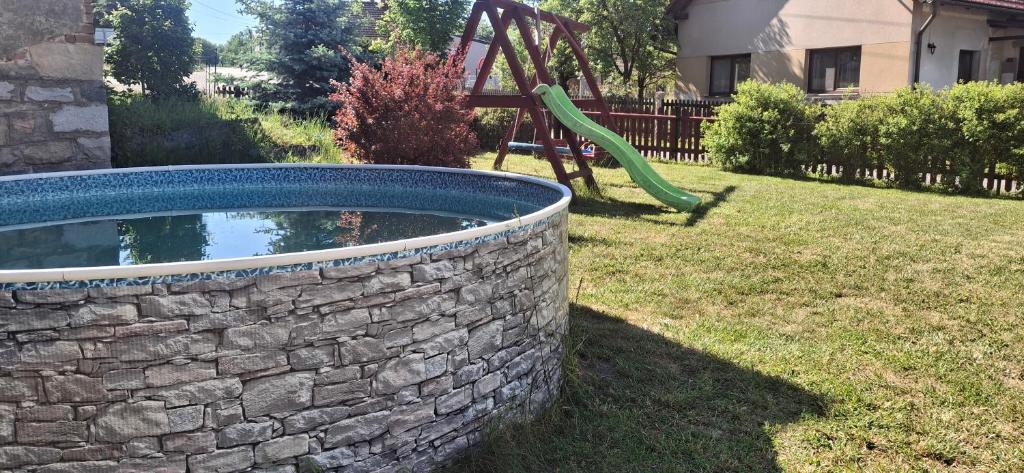 a pool in a yard with a stone wall and a playground at Tisovecký apartmán in Tisovec