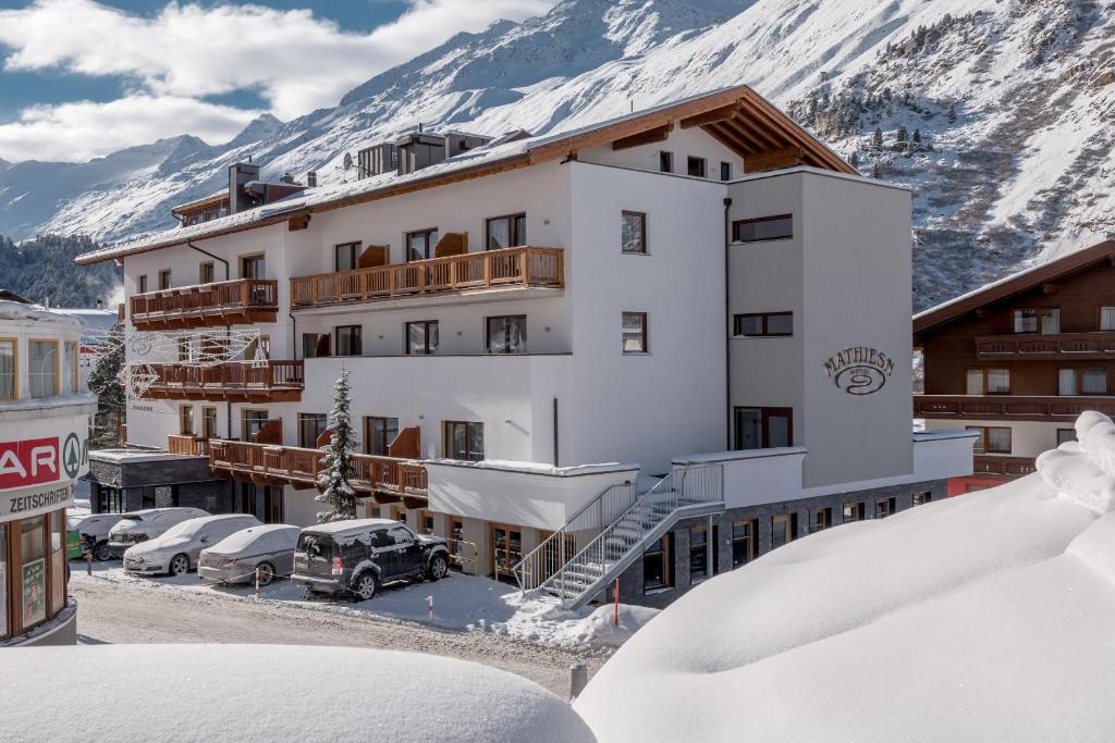 ein Gebäude mit Autos, die draußen im Schnee geparkt sind in der Unterkunft Hotel Mathiesn in Obergurgl