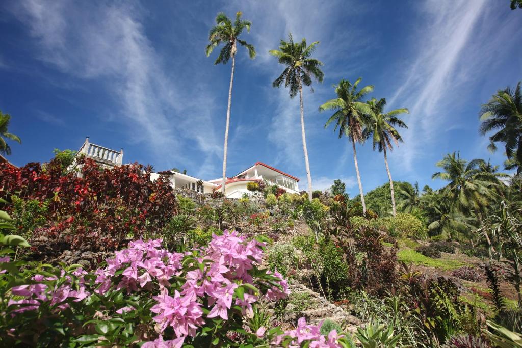 a house on a hill with palm trees and flowers at Guindulman Bay Tourist Inn in Guindulman