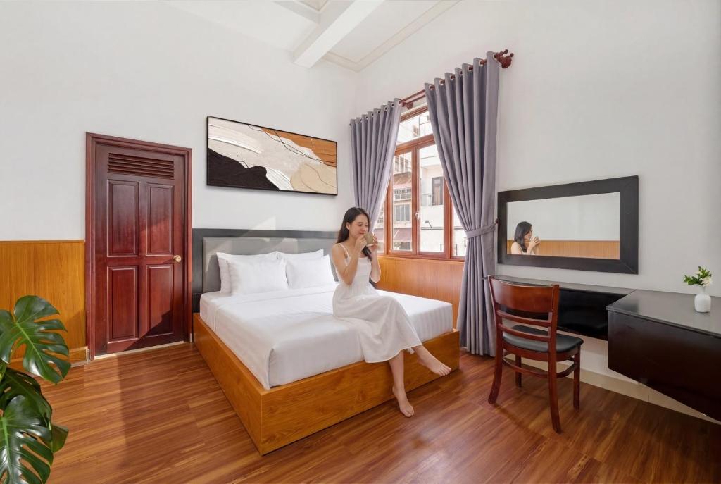 a woman sitting on a bed in a hotel room at Grand Center Da Lat by Lilly Hotel in Da Lat