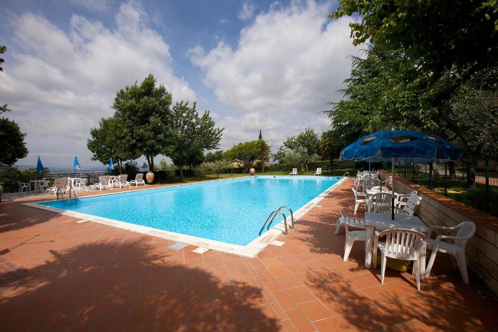 una piscina con mesas, sillas y una sombrilla en Hotel Da Angelo, en Asís