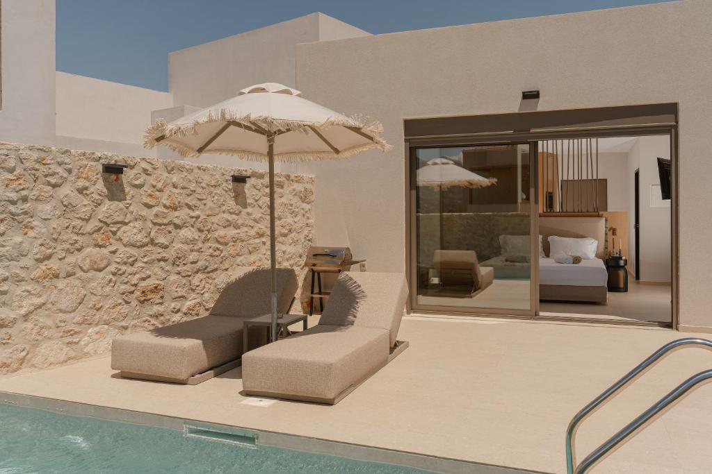 a swimming pool with two chairs and an umbrella at Increteblue Suites in Plakias