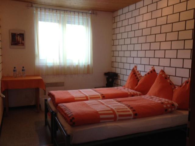 1 dormitorio con 2 camas con almohadas de color naranja y ventana en La Cantina Restaurant, en Alvaneu