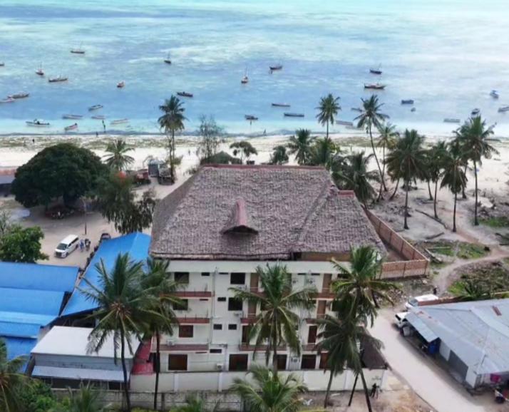 a building on the beach with palm trees and the ocean at Aurora Nungwi in Nungwi