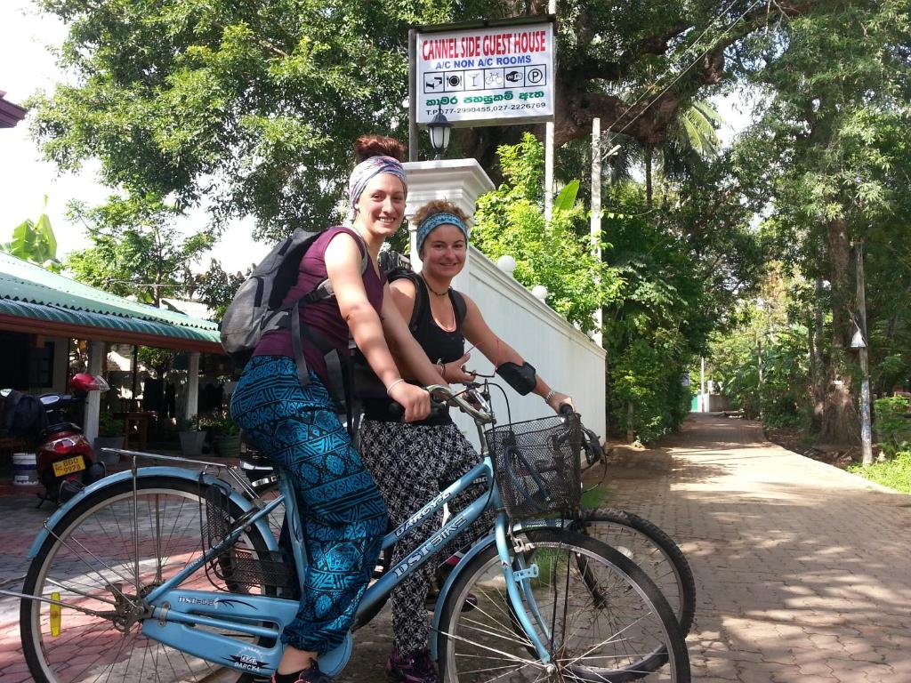 two women are riding a bike down a street at Canal Side Guest House Polonnaruwa in Polonnaruwa