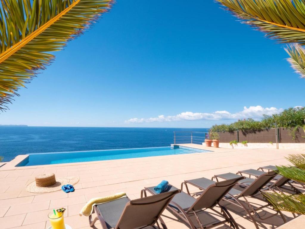 a pool with chairs and the ocean in the background at Villa Sa Troneta in Cala Pi