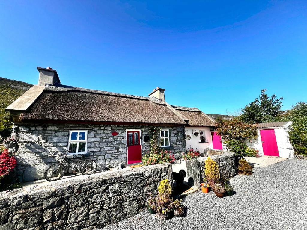 a stone house with red doors and a stone wall at Oranuisce Thatch Cottage Ballyvaughan in Ballyvaughan