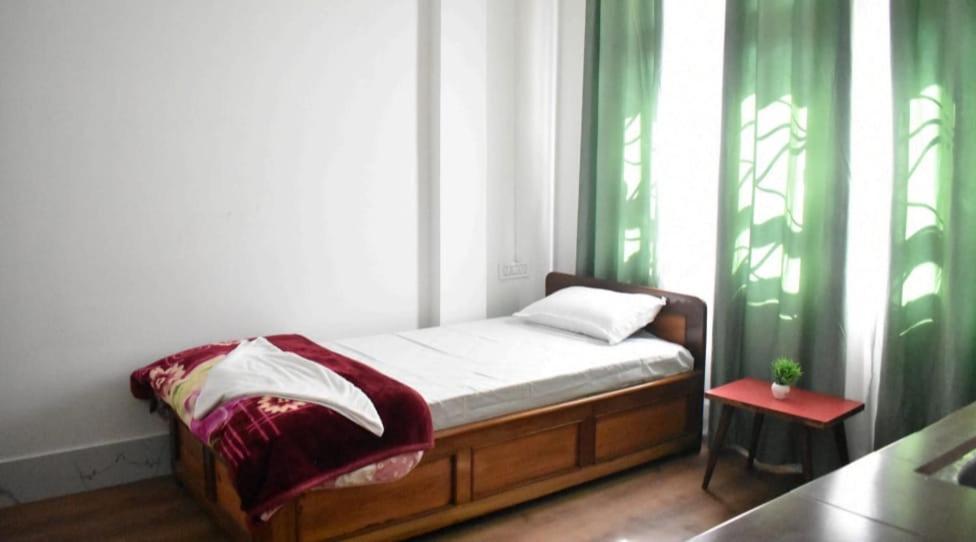 a small bed in a room with green curtains at khim Retreat in Mirik