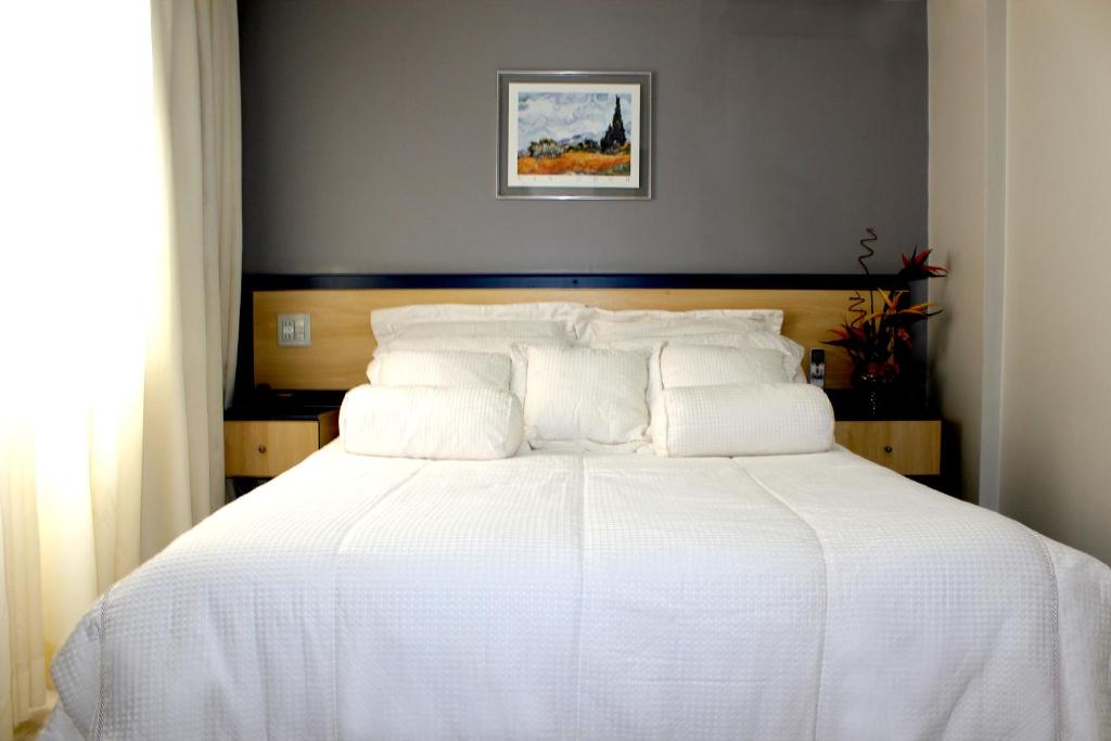 a bedroom with a white bed with a wooden headboard at La Défense Apart Hotel in Montes Claros