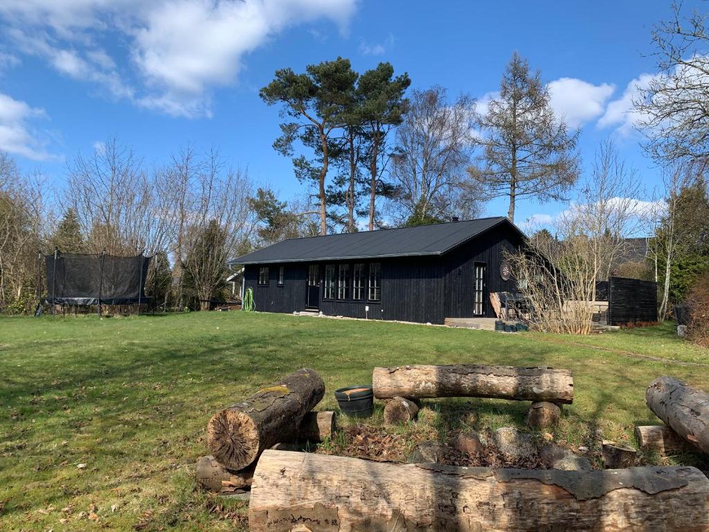 a black building in a field with logs in front at Charming Holiday Home At Sought-After Tisvilde in Vejby
