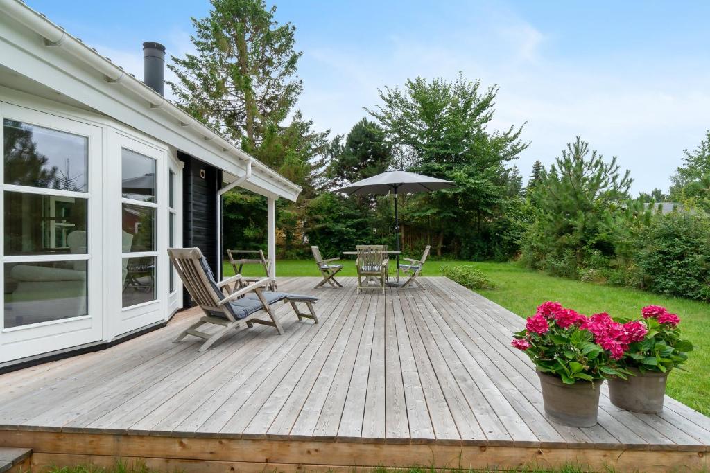 a wooden deck with chairs and an umbrella at Summer Cottage With Jacuzzi And Sauna in Fakse Ladeplads