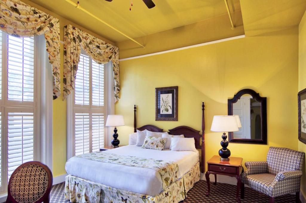 a bedroom with a bed and a chair and windows at Menger Hotel in San Antonio