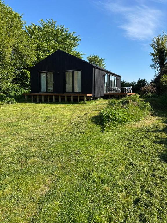 a black house sitting on top of a grass field at Stylish Cottage Near Beach Cliffs Harbour in Havnelev
