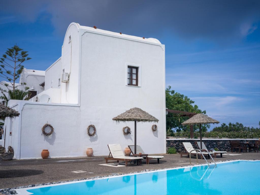 a white building with chairs and a swimming pool at Anna Traditional Apartments in Kamari