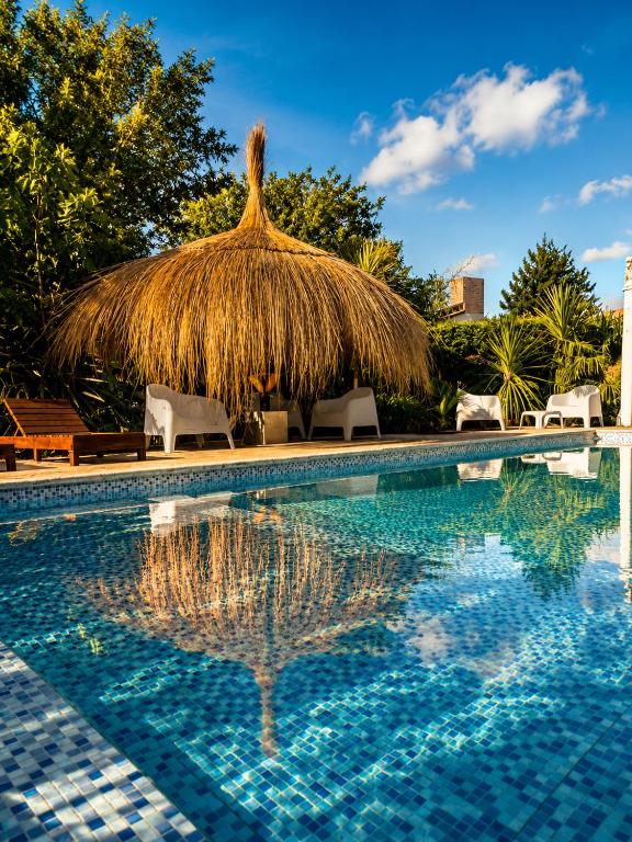 a resort swimming pool with a thatched roof and chairs at Algarrobos del Mirador in Santa Rosa de Calamuchita