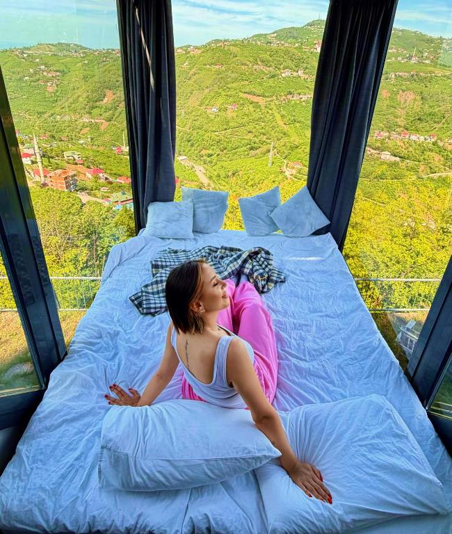 a woman laying on a bed in a window at Lazord Glass Bungalow Trabzon in Geçit