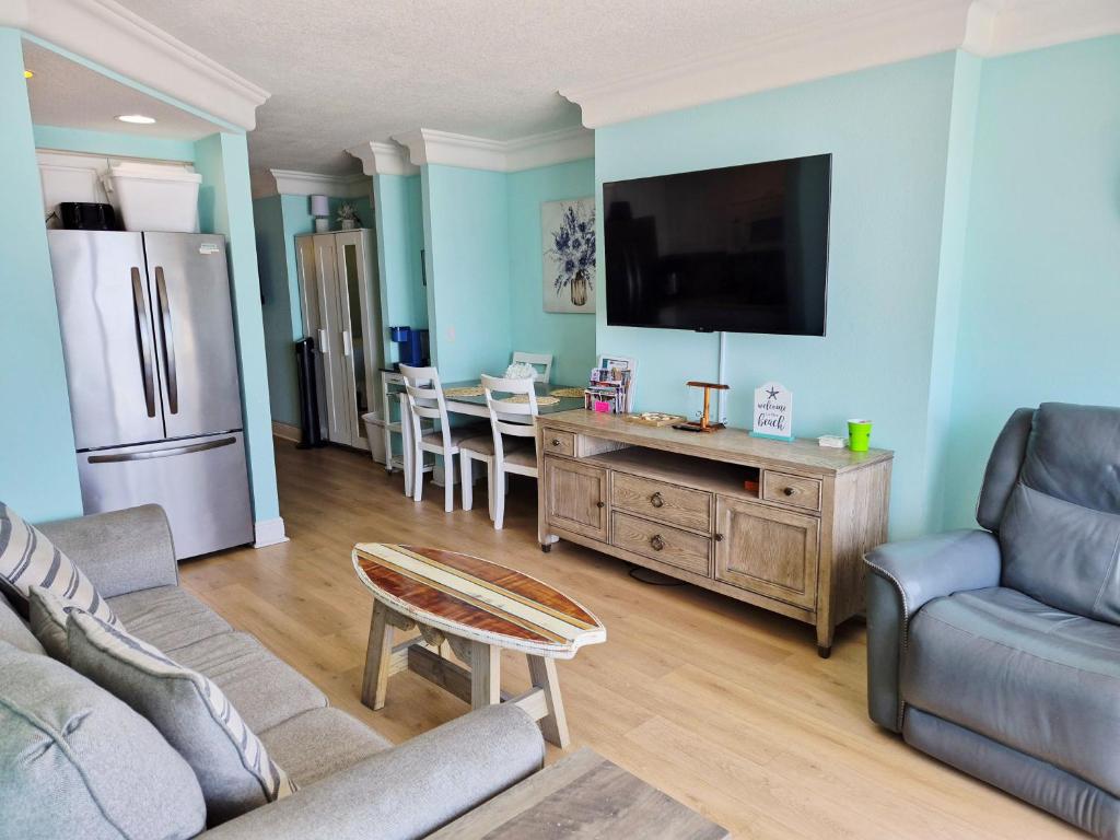 a living room with a couch and a tv and a table at Sunkissed-Modern Oceanfront Condo Daytona Beach in Daytona Beach