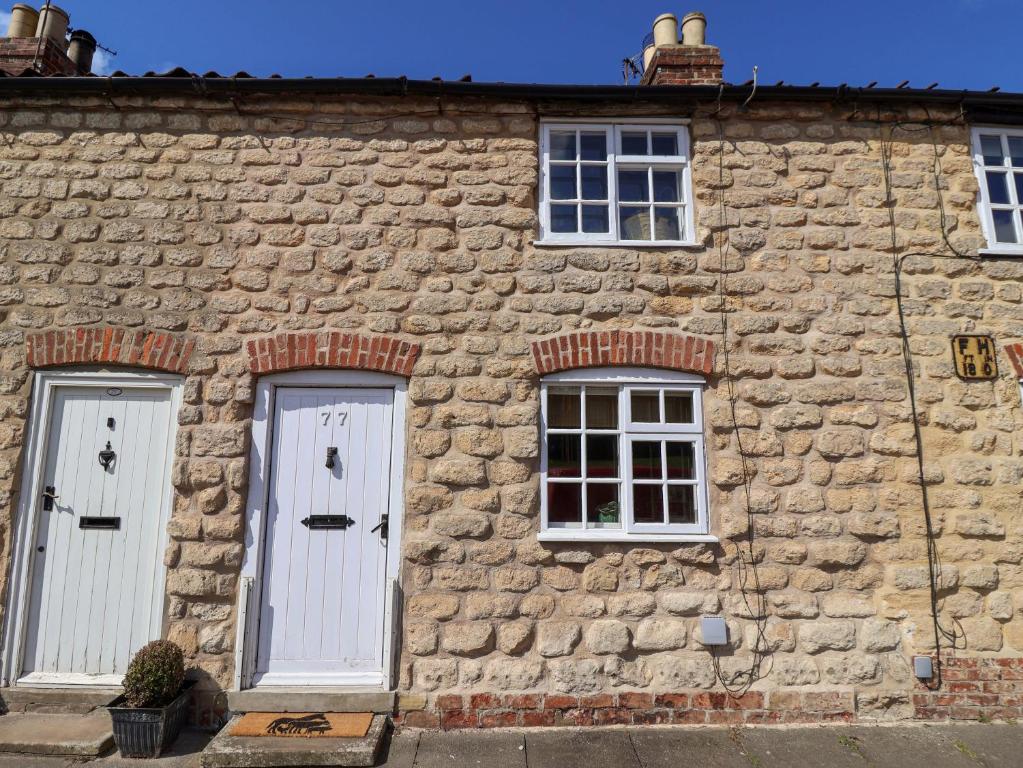 a stone building with two white doors and two windows at The Cooks Cottage in Malton