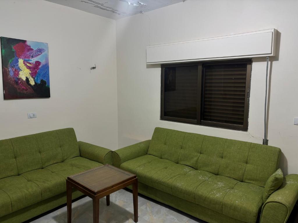 a living room with two green couches and a window at Ahmmad Alshgoor in Şirfah