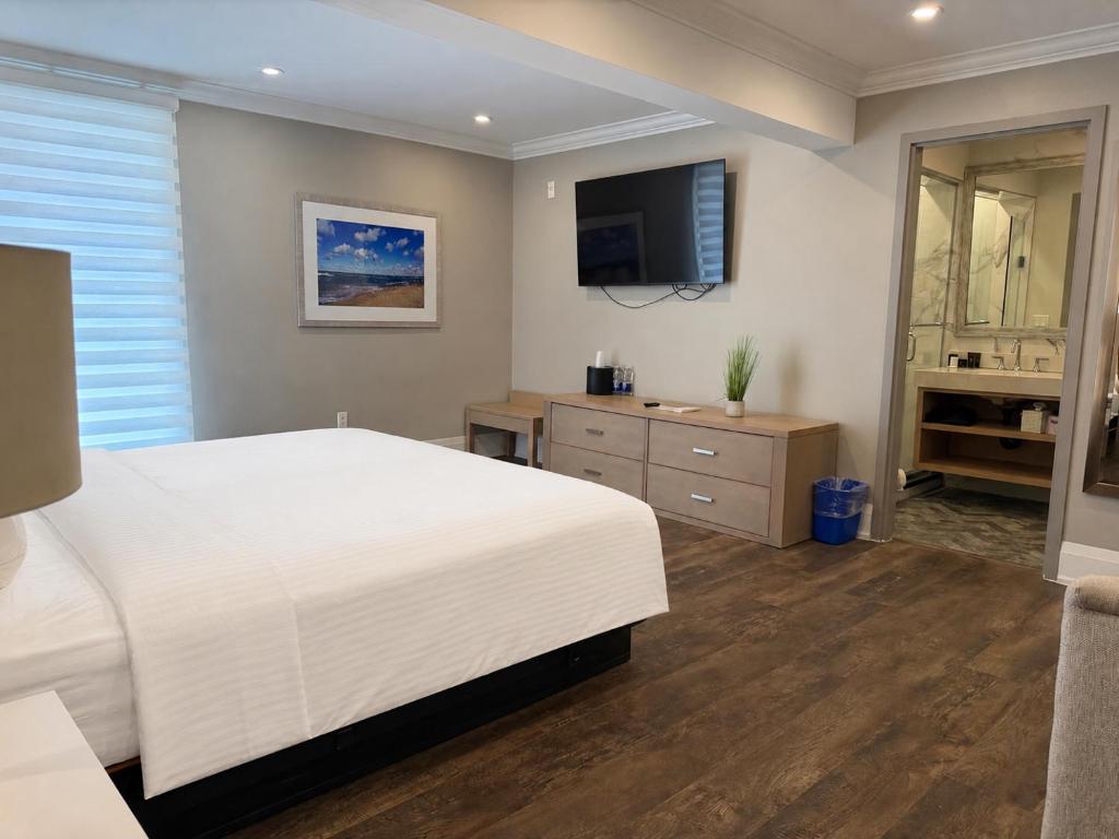 a bedroom with a white bed and a flat screen tv at Colonial Hotel & Suites in Grand Bend