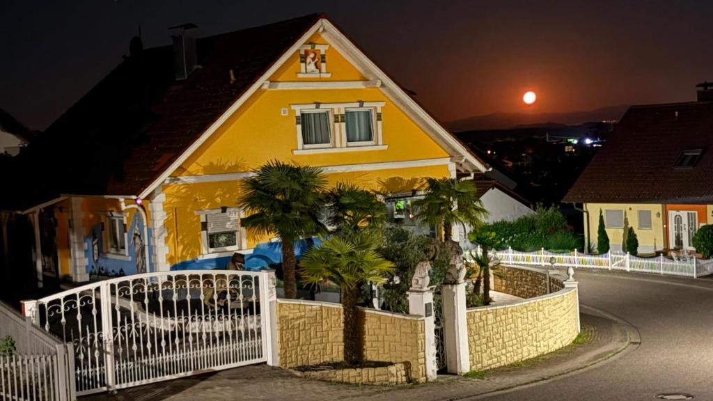 a yellow house with a white fence and palm trees at Casa Kovacs in Herbolzheim