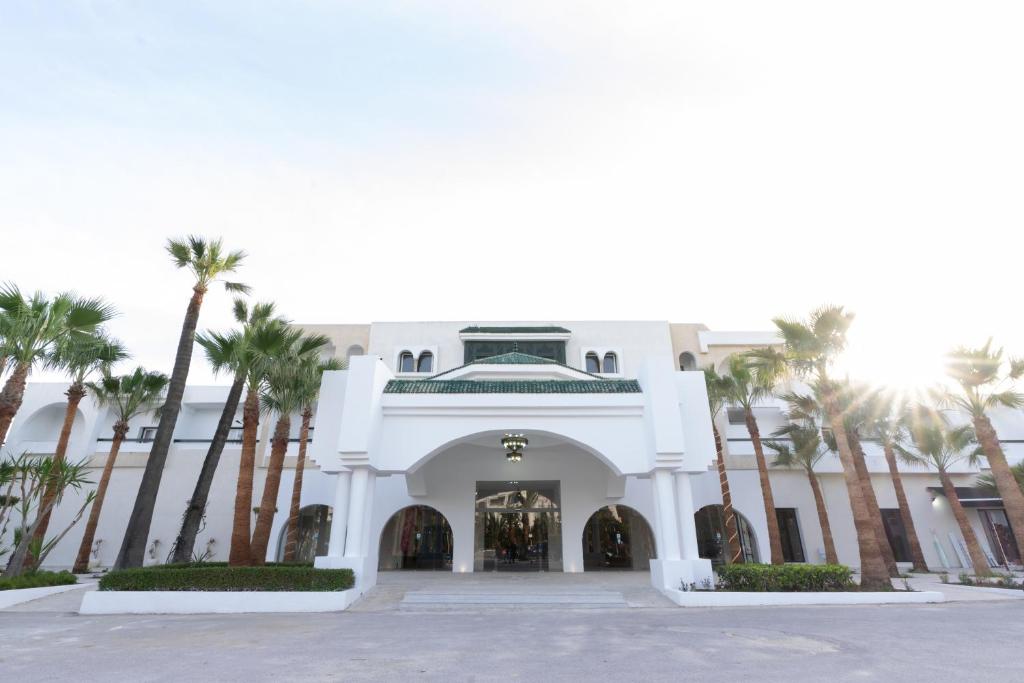 a white building with palm trees in front of it at Hôtel Hammamet Beach in Hammamet