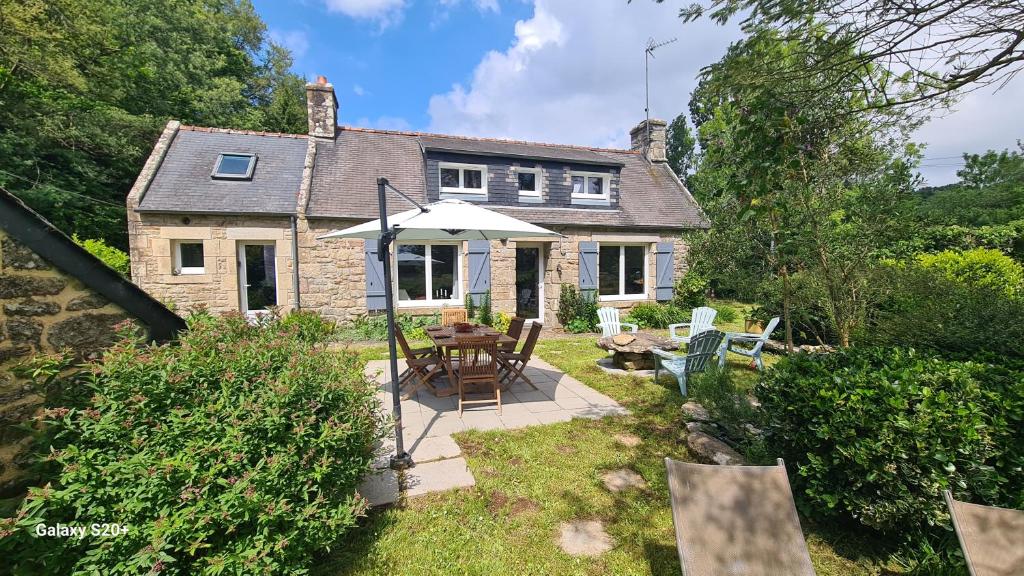 a house with a table and an umbrella in the yard at le moulin in Pont-Croix