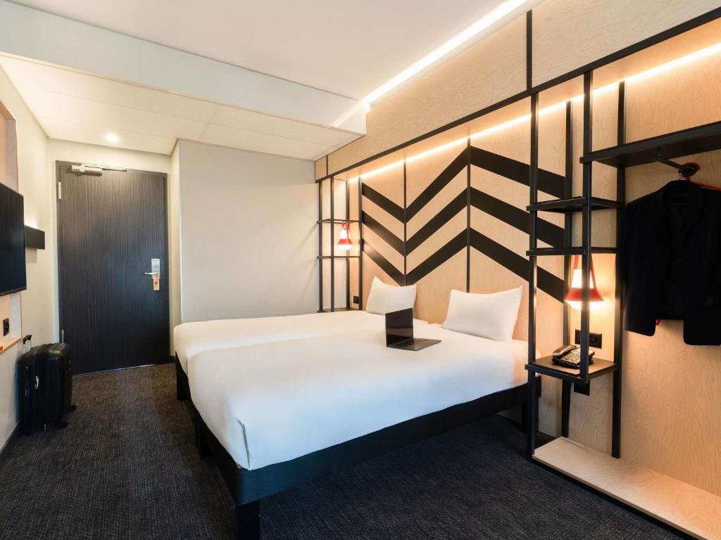 a hotel room with a large white bed and a shelf at ibis Styles Geneve Palexpo Aeroport in Geneva