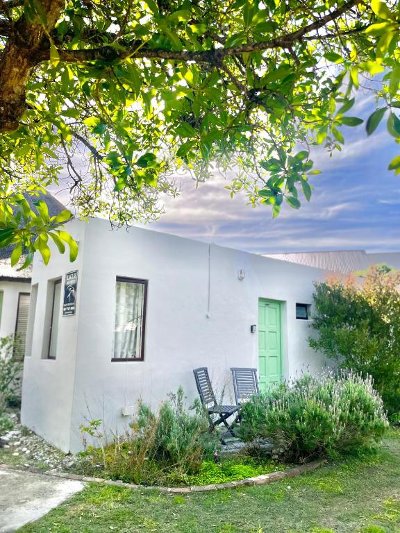 a white house with a green door and two chairs at Kelp Cottage - Two Private Garden en-suite Rooms in Gansbaai