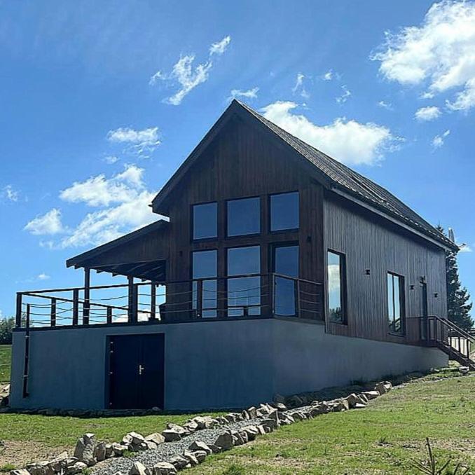 a large wooden house with a porch on a field at Hill House Marisel in Mărişel