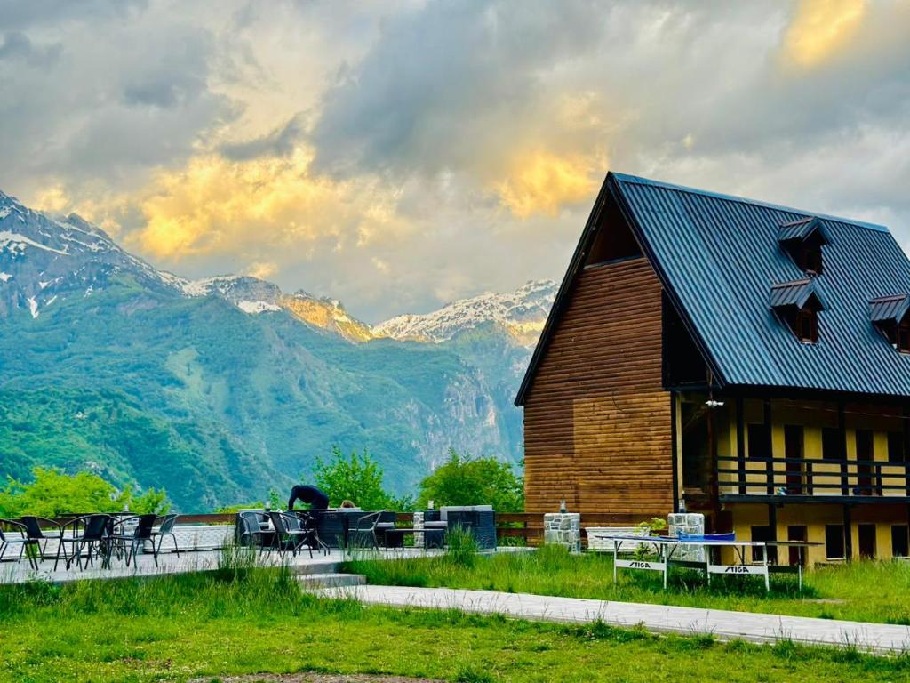 a wooden barn with tables and chairs in front of mountains at Guesthouse Gjoni Theth in Theth