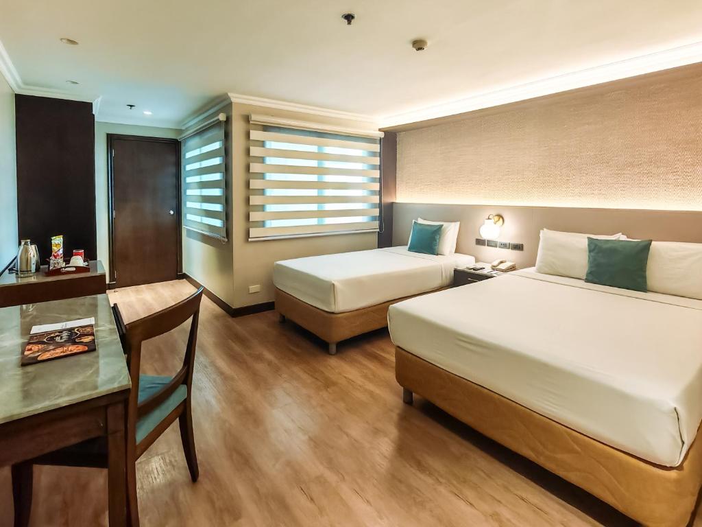 a hotel room with two beds and a table and a desk at City Garden Suites Manila in Manila